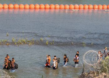 Migrants walk between concertina wire and a string of buoys in the Rio Grande at Eagle Pass, Texas / ©AFP