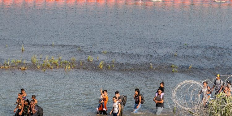 Migrants walk between concertina wire and a string of buoys in the Rio Grande at Eagle Pass, Texas / ©AFP