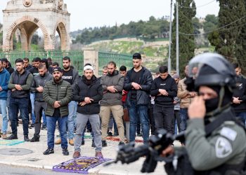 Israeli security forces stand guard as Palestinian Muslims perform Friday Noon prayers on a street in east Jerusalem on February 23, 2024 / ©AFP