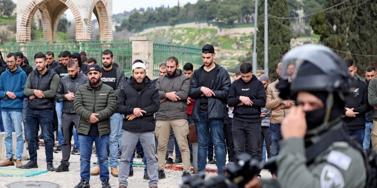 Israeli security forces stand guard as Palestinian Muslims perform Friday Noon prayers on a street in east Jerusalem on February 23, 2024 / ©AFP