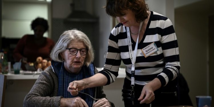 A health care worker (R) tends helps a patient with Alzheimer's eat lunch. ©AFP