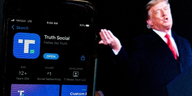 Donald Trump next to a phone screen displaying the Truth Social app / ©AFP