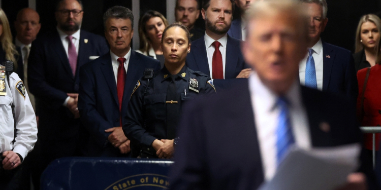 Senator JD Vance (center, red tie), Senator Tommy Tuberville (back right, blue tie) and Eric Trump (center back) look on as former US president Donald Trump speaks to reporters at his trial for allegedly covering up hush money payments / ©AFP