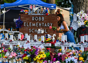 A girl lays flowers at a makeshift memorial at Robb Elementary School in Uvalde, Texas in May 2022. ©AFP