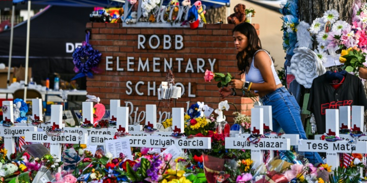 A girl lays flowers at a makeshift memorial at Robb Elementary School in Uvalde, Texas in May 2022. ©AFP