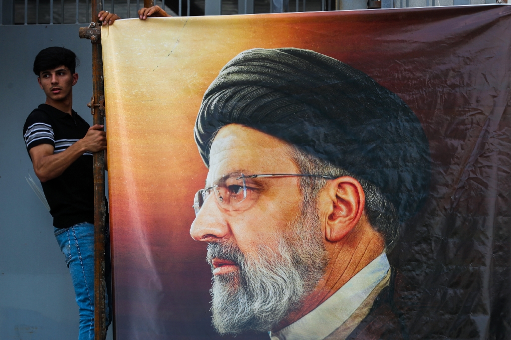 Men hang a huge portrait of Iran's late president Ebrahim Raisi outside the Iranian embassy in Baghdad  / ©AFP