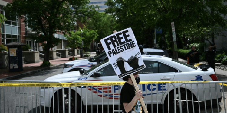 A demonstrator holds a sign as a police vehicle and barricades block a road after officers cleared a pro-Palestinian student protest encampment at George Washington University on May 8, 2024. ©AFP