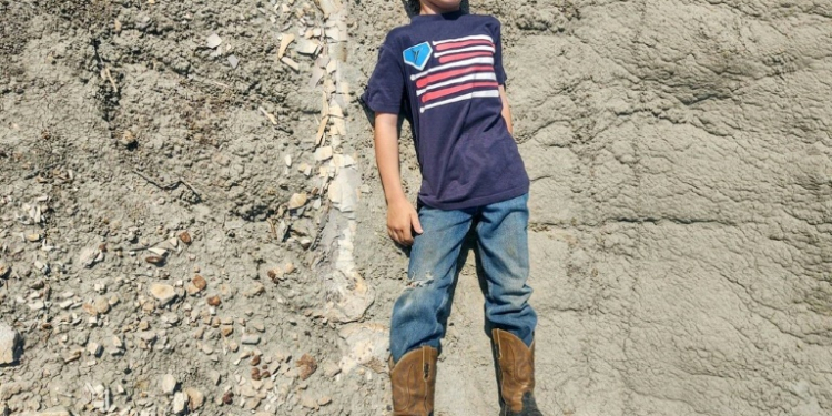 Young Liam Fisher lay down next to the fossilized leg bone of a dinosaur he discovered in the Badlands of North Dakota in 2022, and his family sent the photograph to a paleontologist friend, who confirmed it to be of a juvenile Tyrannosaurus rex. ©AFP