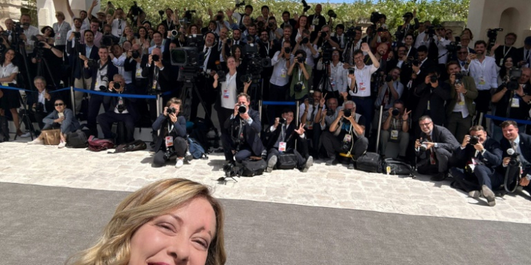 This handout picture released by Meloni's office shows Prime Minister Giorgia Meloni shooting a selfie with the press. ©AFP