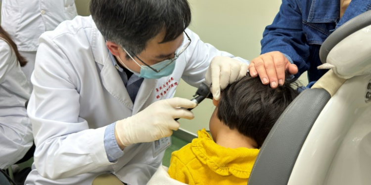 This handout picture courtesy of the Eye & Ent Hospital of Fudan University shows Dr Yilai Shu examining a young patient at the Eye & ENT Hospital of Fudan University in this image taken on April 17, 2024. ©AFP