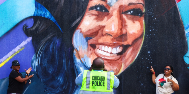 A Chicago police officer photographs people posing before a mural of US Vice President Kamala Harris outside the United Center ahead of the Democratic National Convention / ©AFP