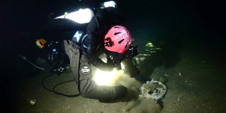 A handout image from Atlantic Wreck Salvage shows diver Joe Mazraani fanning away sand to reveal a 'deadeye' used as part of the sail rigging of Le Lyonnais. ©AFP