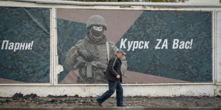 A man walks past a wall adorned with banners honouring Russian servicemen participating in Russia's military action in Ukraine. ©AFP