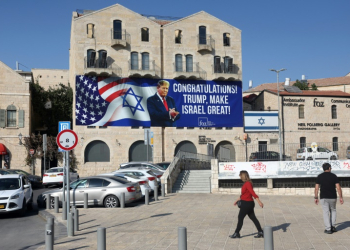 People in Jerusalem walk past a billboard congratulating US President-elect Donald Trump on November 8, 2024. ©AFP