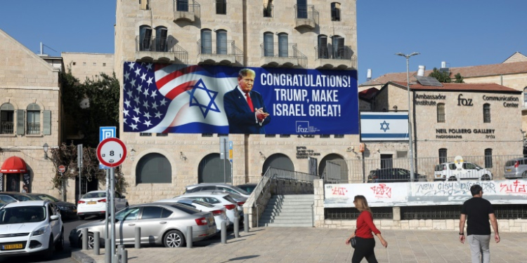 People in Jerusalem walk past a billboard congratulating US President-elect Donald Trump on November 8, 2024. ©AFP