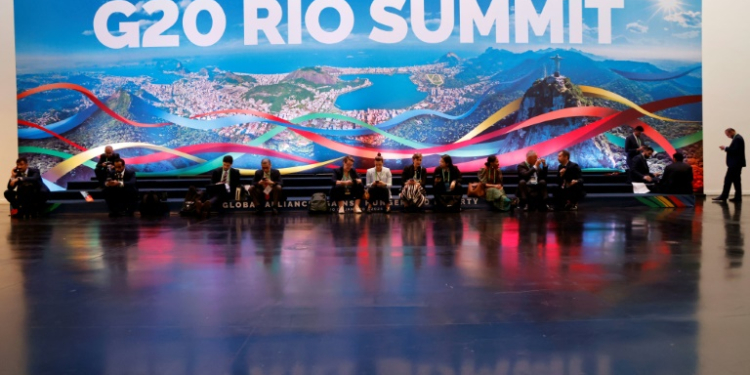 People sit and work next to a giant banner of the G20 Summit in Rio de Janeiro, Brazil, on November 18, 2024. ©AFP