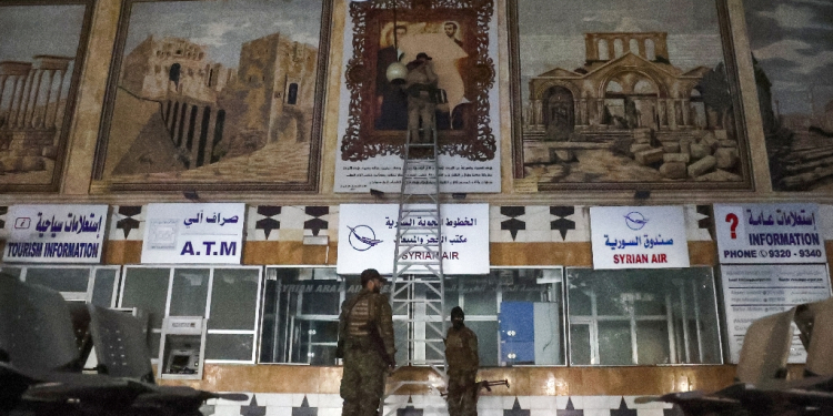 Anti-regime fighters tear off a poster depicting Syrian President Bachar al-Assad and his brother Maher at the airport in the northern Syrian city of Aleppo / ©AFP