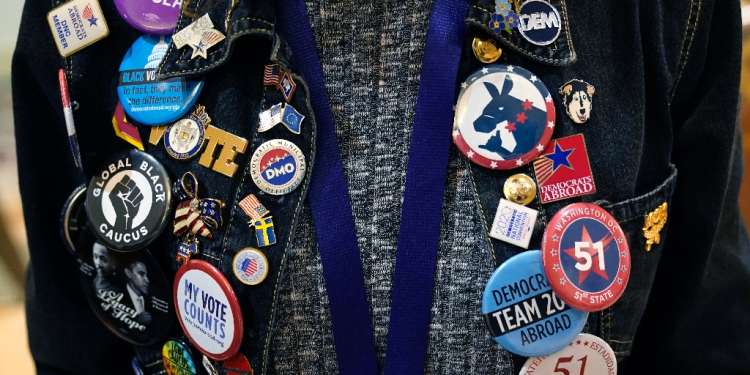 A woman shows off her button and pin collection during day one of the Democratic National Committee 2023 Winter meeting / ©AFP